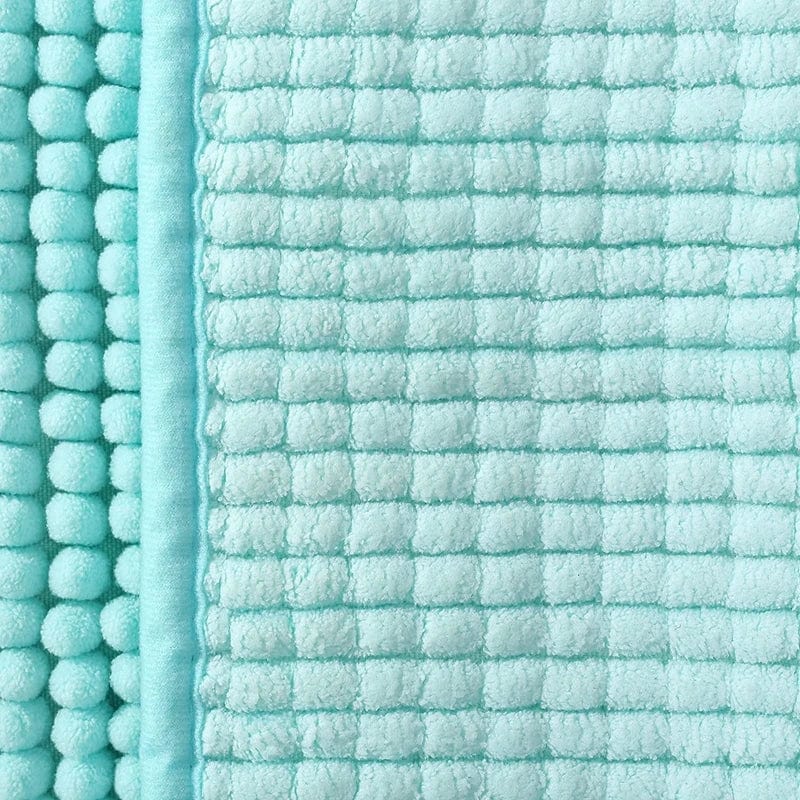 Turquoise badmat met kruispatroon en pomponrand, stijlvolle badkamer tapijt.