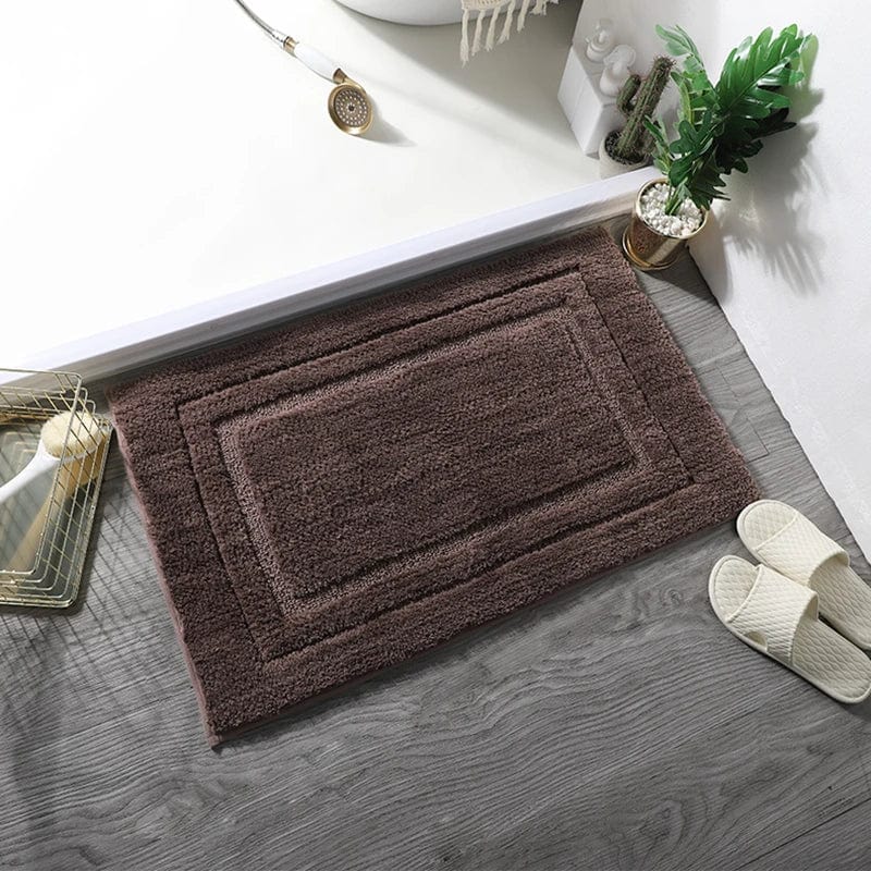Absorbent bath mat in brown, placed beside bathtub with slippers and plant.