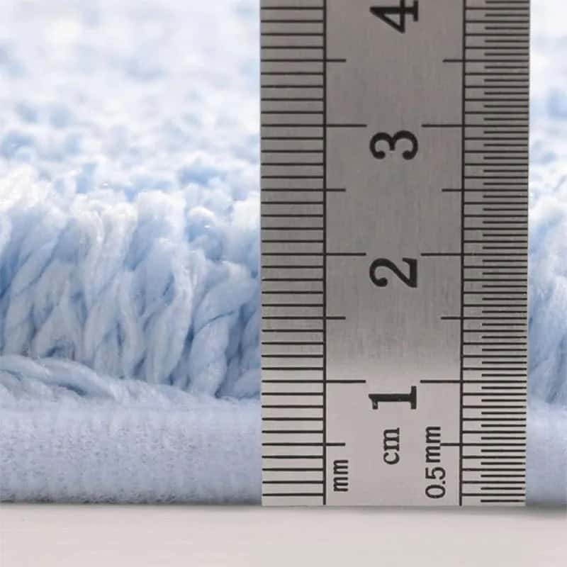 Close-up of artsy bath mat texture with ruler showing thickness measurement.