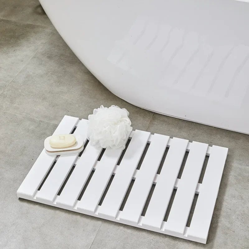 White bamboo slatted bath mat with soap and loofah beside bathtub.