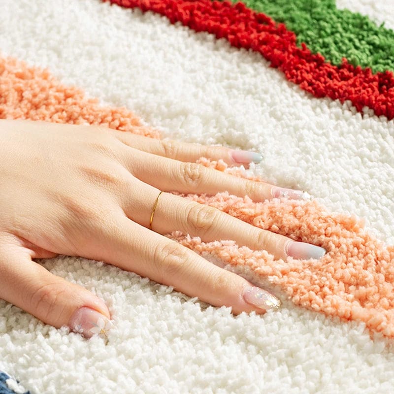 Hand resting on colourful fluffy bath mat with red, green and peach stripes.