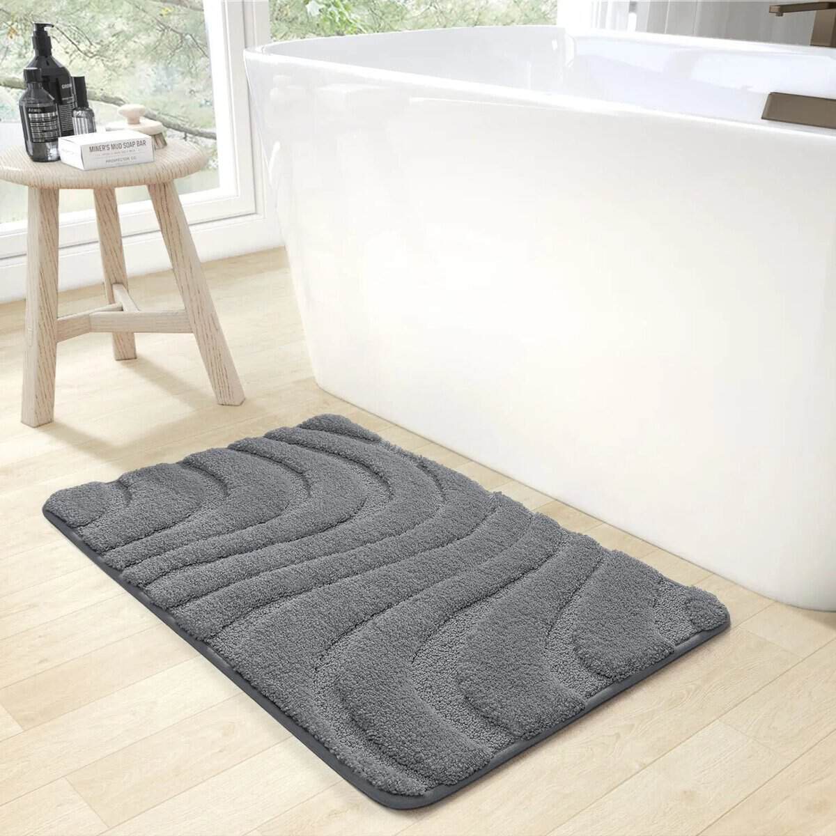 Dark grey textured bath mat beside white freestanding bathtub.