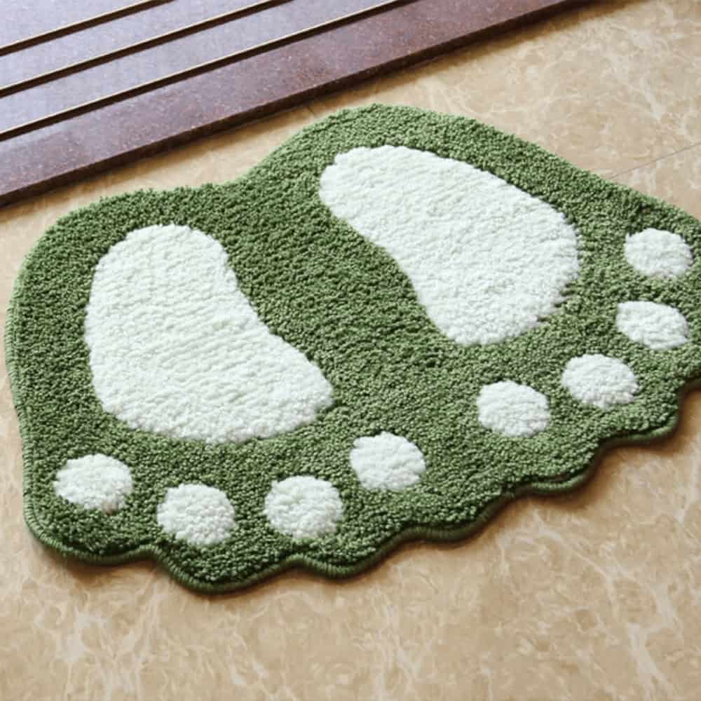 Green foot-shaped bath mat with white paw print design for bathroom.