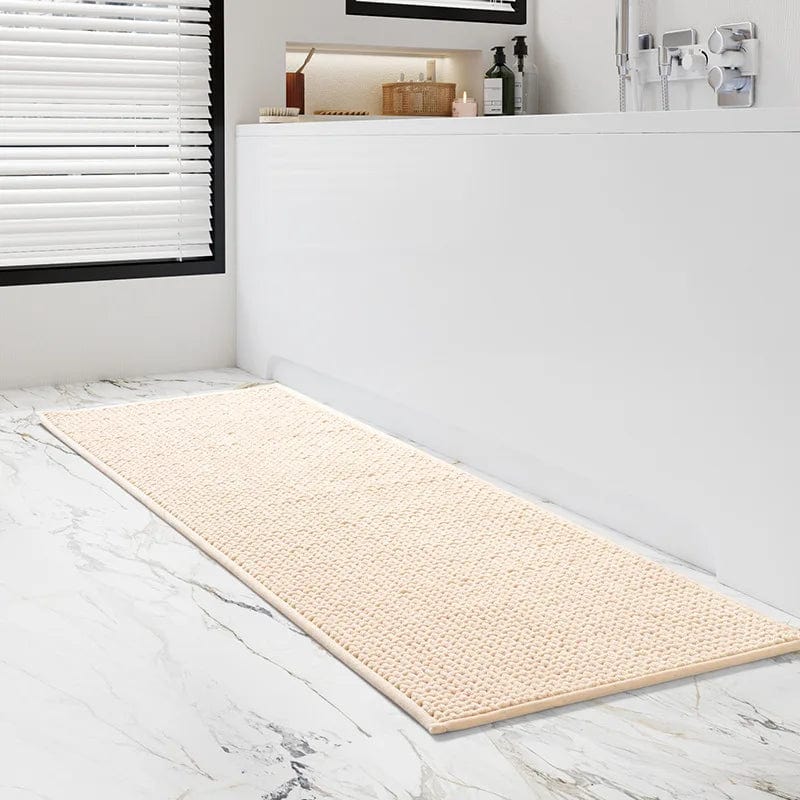 Cream textured bath mat on marble floor beside white bathtub.