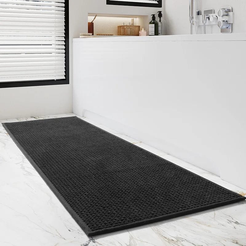 Black textured bath mat on marble floor in modern bathroom.