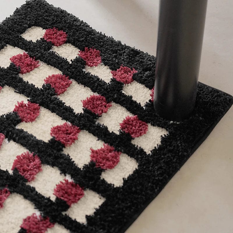 Geometric bath mat with black, white, and pink pom-pom pattern.