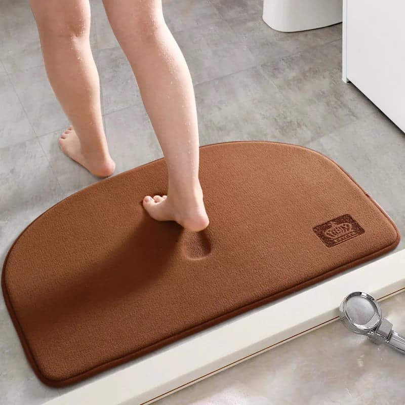Brown halfmoon bath mat with crown logo, person stepping on it.