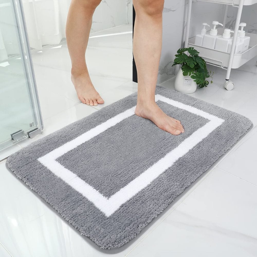 Large absorbent grey bath mat with white border for bathroom comfort.