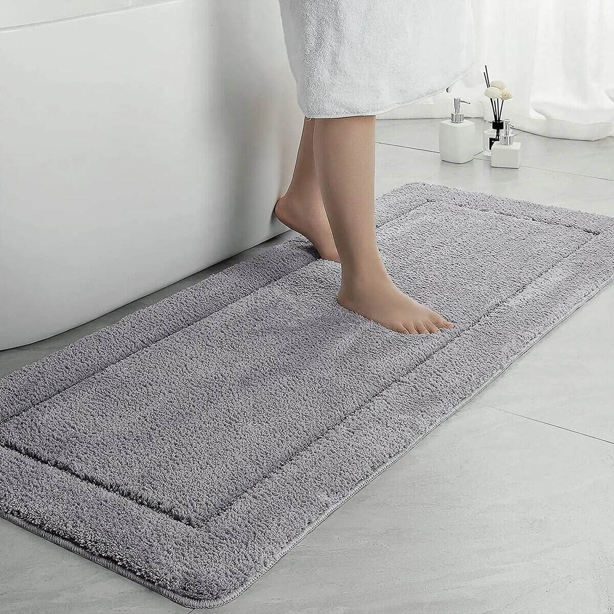 Large grey fluffy bath mat with person stepping on it near bathtub.