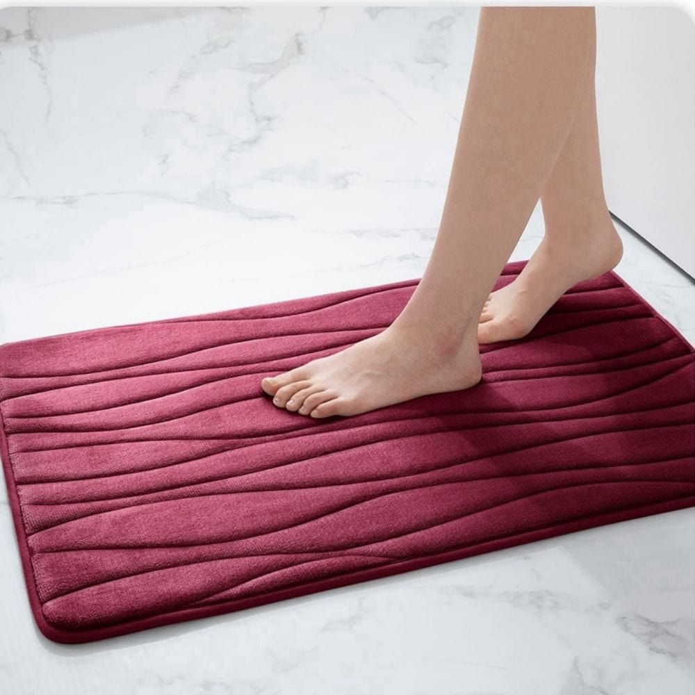 Large water absorbent bath mat in burgundy, feet standing on textured surface.