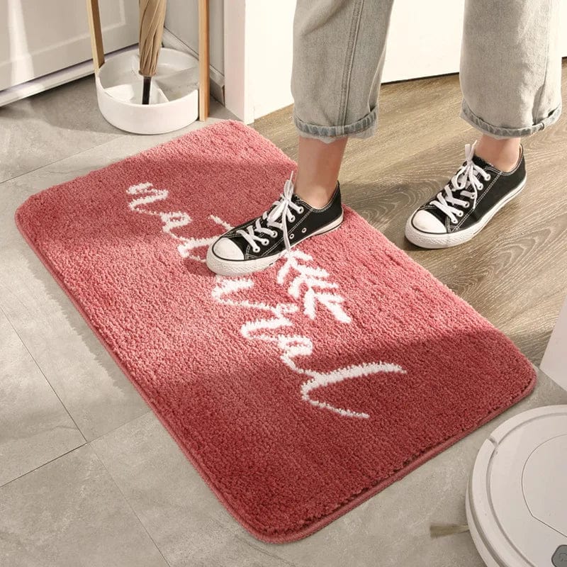 Pink fluffy bath mat with 'Natural' text design, cozy bathroom rug.