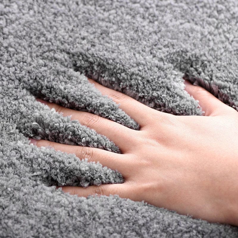Soft grey non-slip bath mat with hand touching plush texture.