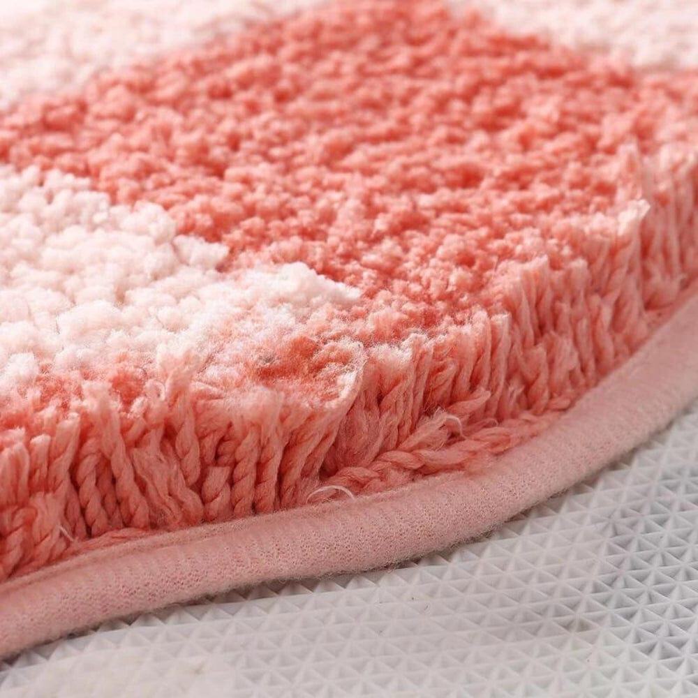 Soft pink gradient bath mat with plush texture and fringed edge.