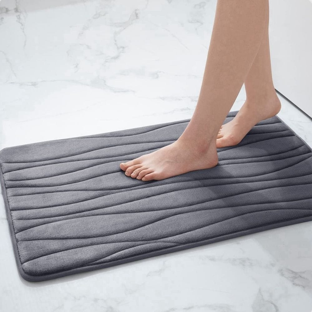 Gray textured bath mat for small bathrooms with feet stepping on it.