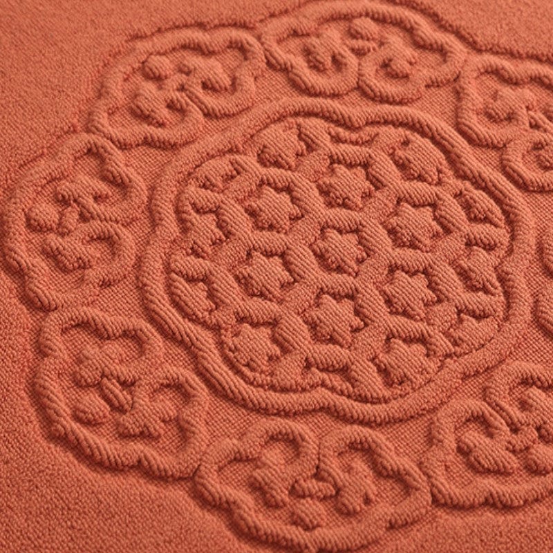 Thick cotton bath mat with intricate floral embroidery in terracotta.