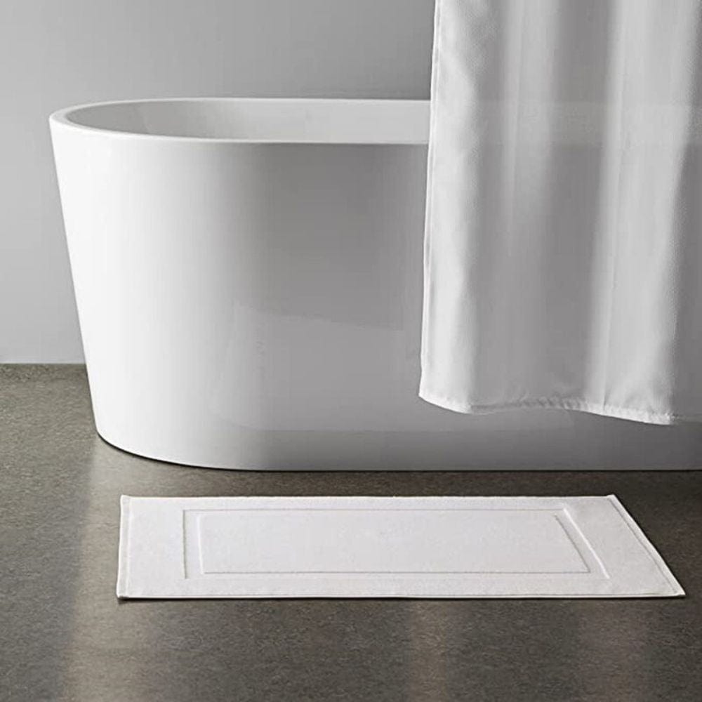 White cotton bath mat beside modern freestanding bathtub.